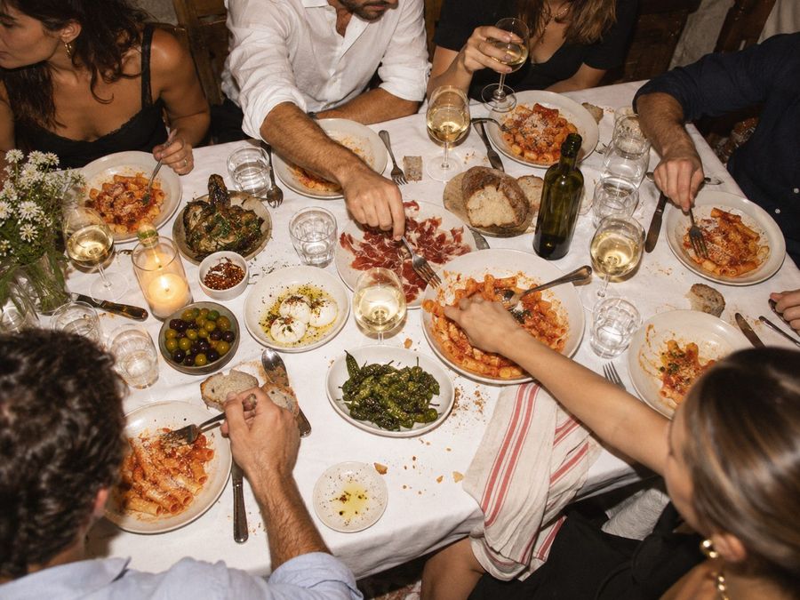 Overhead view of a shared table with pasta, jamón and wine